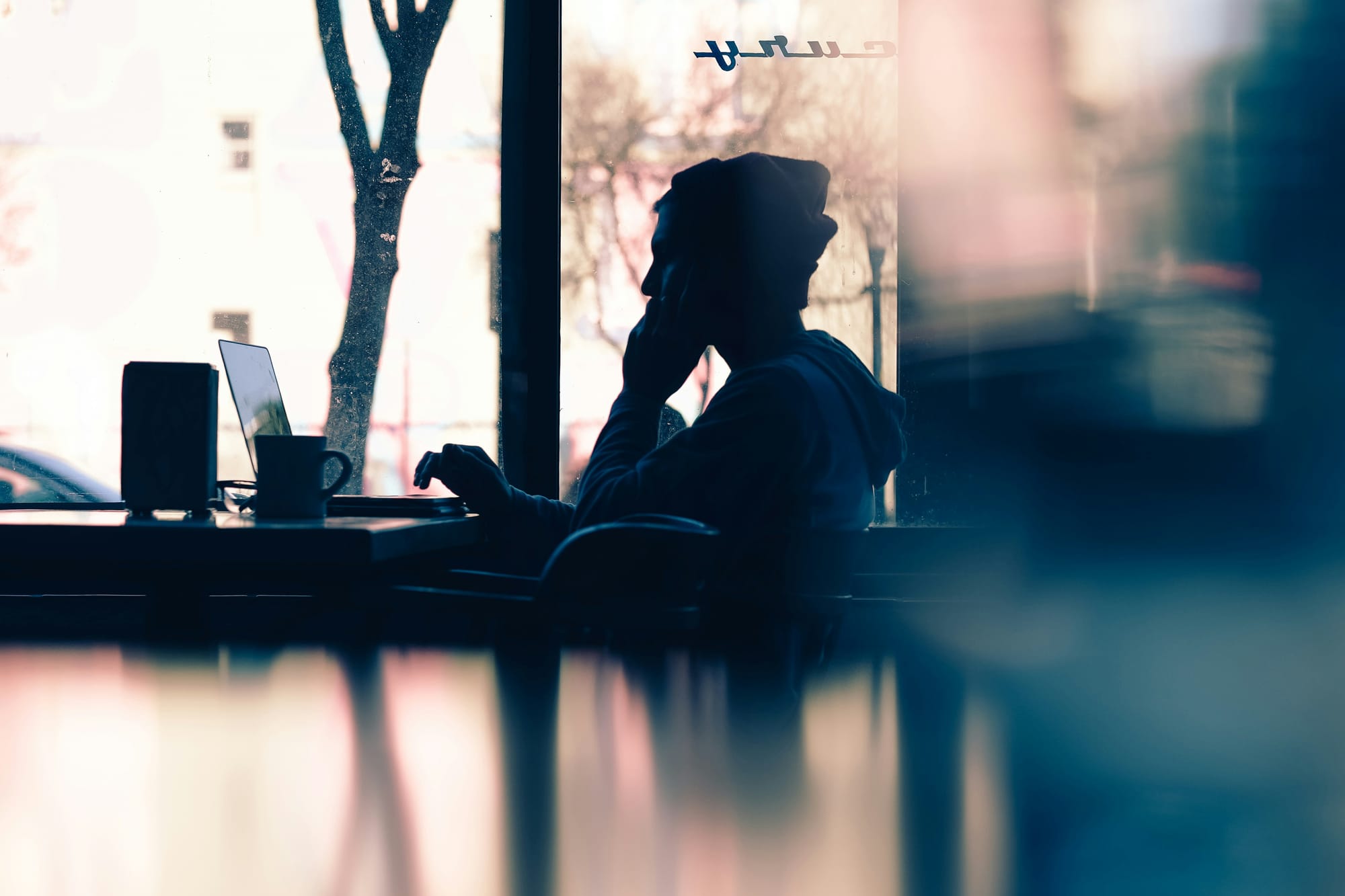 Someone working on a computer in a dusky room with the sunset being reflected on the tabletop next to them