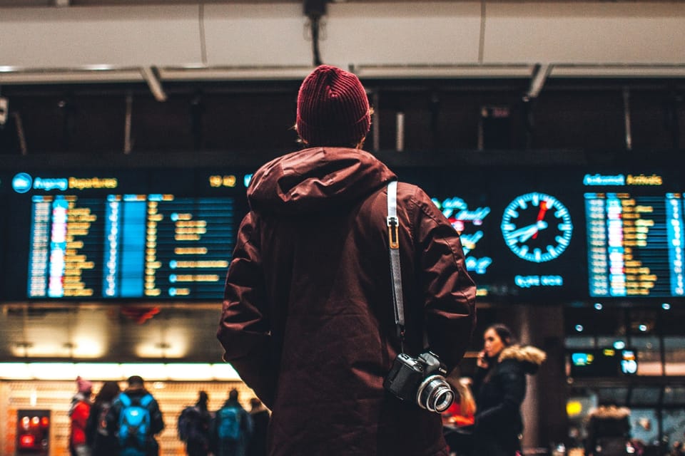 Someone looking at the departure board at the airport, with a camera around their shoulder